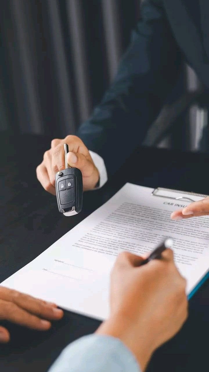 An insurance agent handing over car keys while a customer signs a policy document